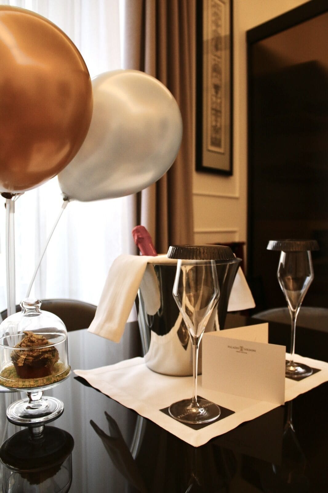 A hotel room with a table set for a meal, including a glass of wine, a bottle of wine, a glass of water, and a menu.