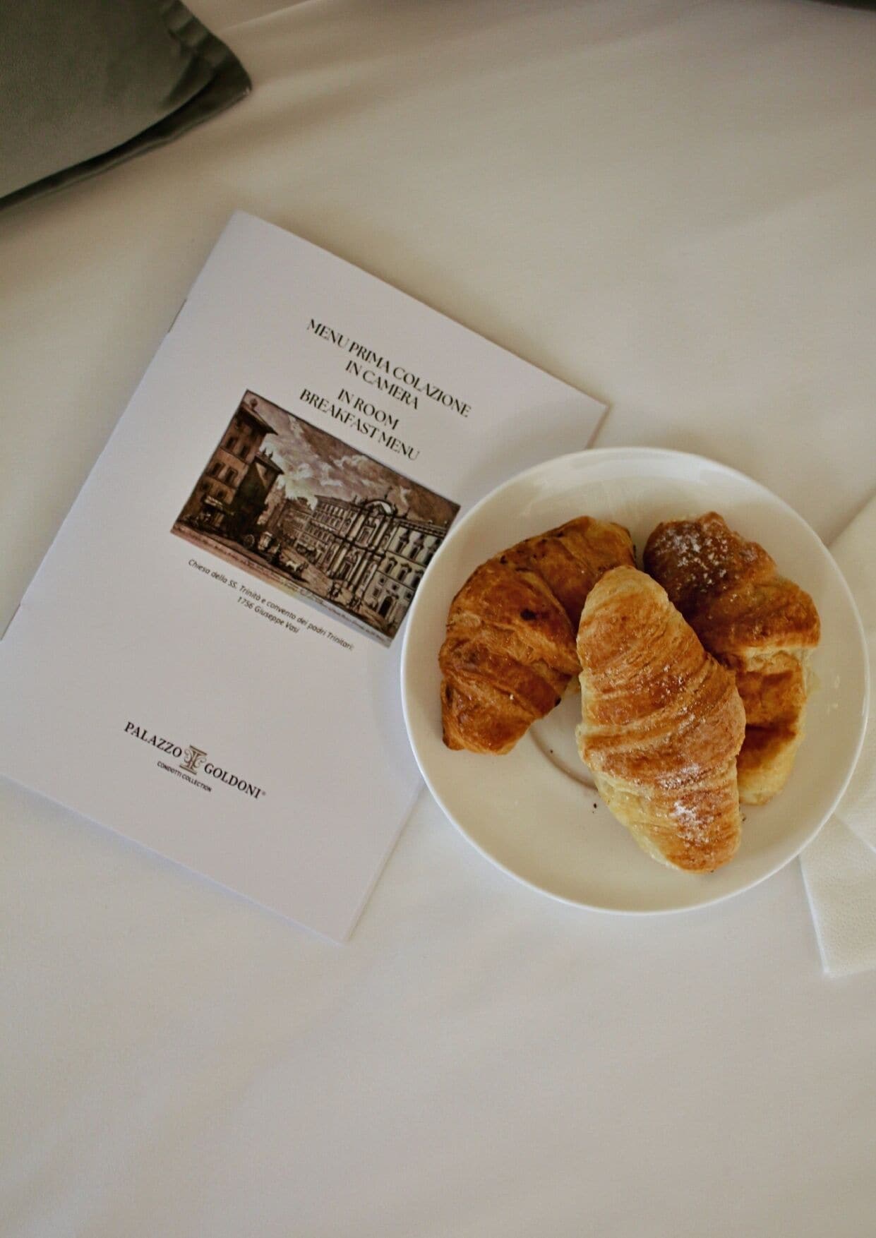 Un menú de desayuno con una foto de un edificio histórico, un plato de cruasanes y el logotipo de Palazzo Goldoni.