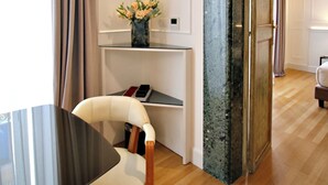 A modern room with a wooden floor, a glass table, a white chair, a shelf with a vase of flowers, and a door leading to another room. - Palazzo Goldoni Condotti Collection (Rome)