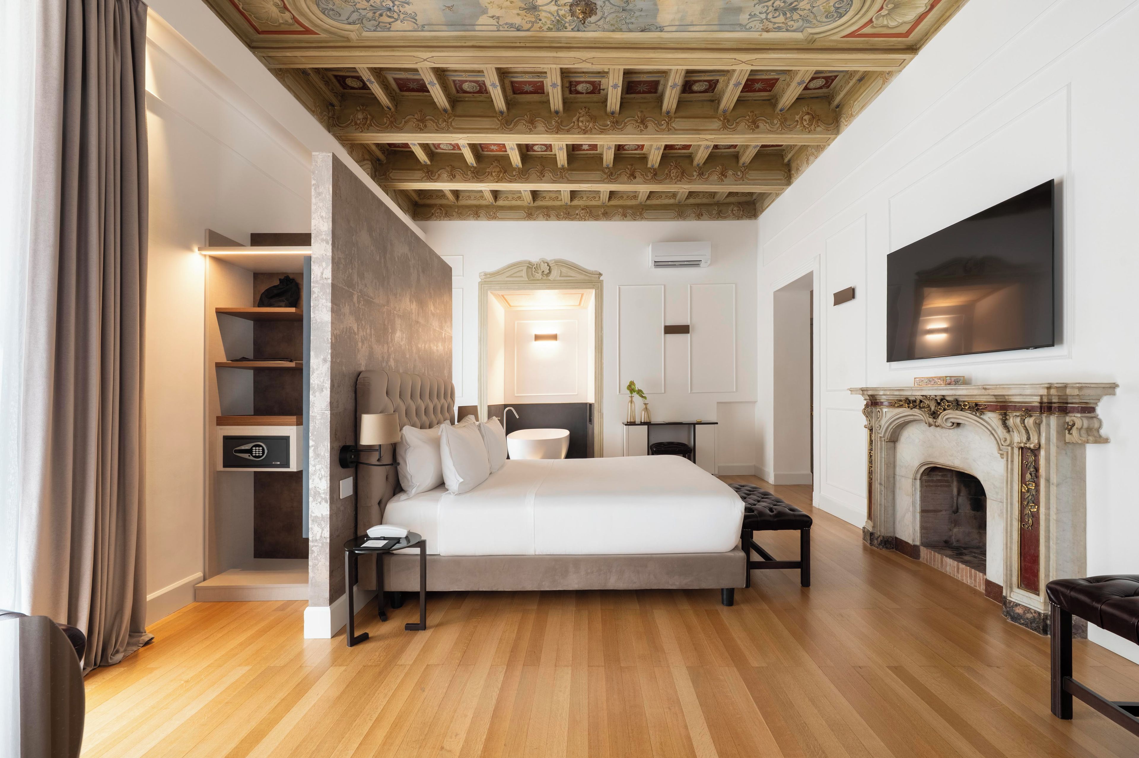 A hotel room with a bed, bedside tables, a fireplace, and a television.