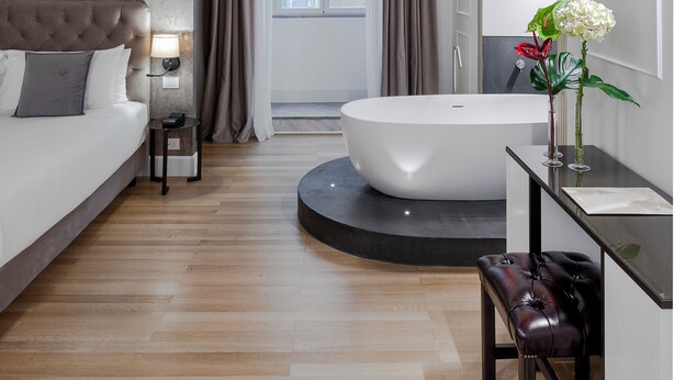 A modern bedroom with a large bed, a bathtub, and a vanity with a mirror. - Palazzo Goldoni Condotti Collection (Rome)