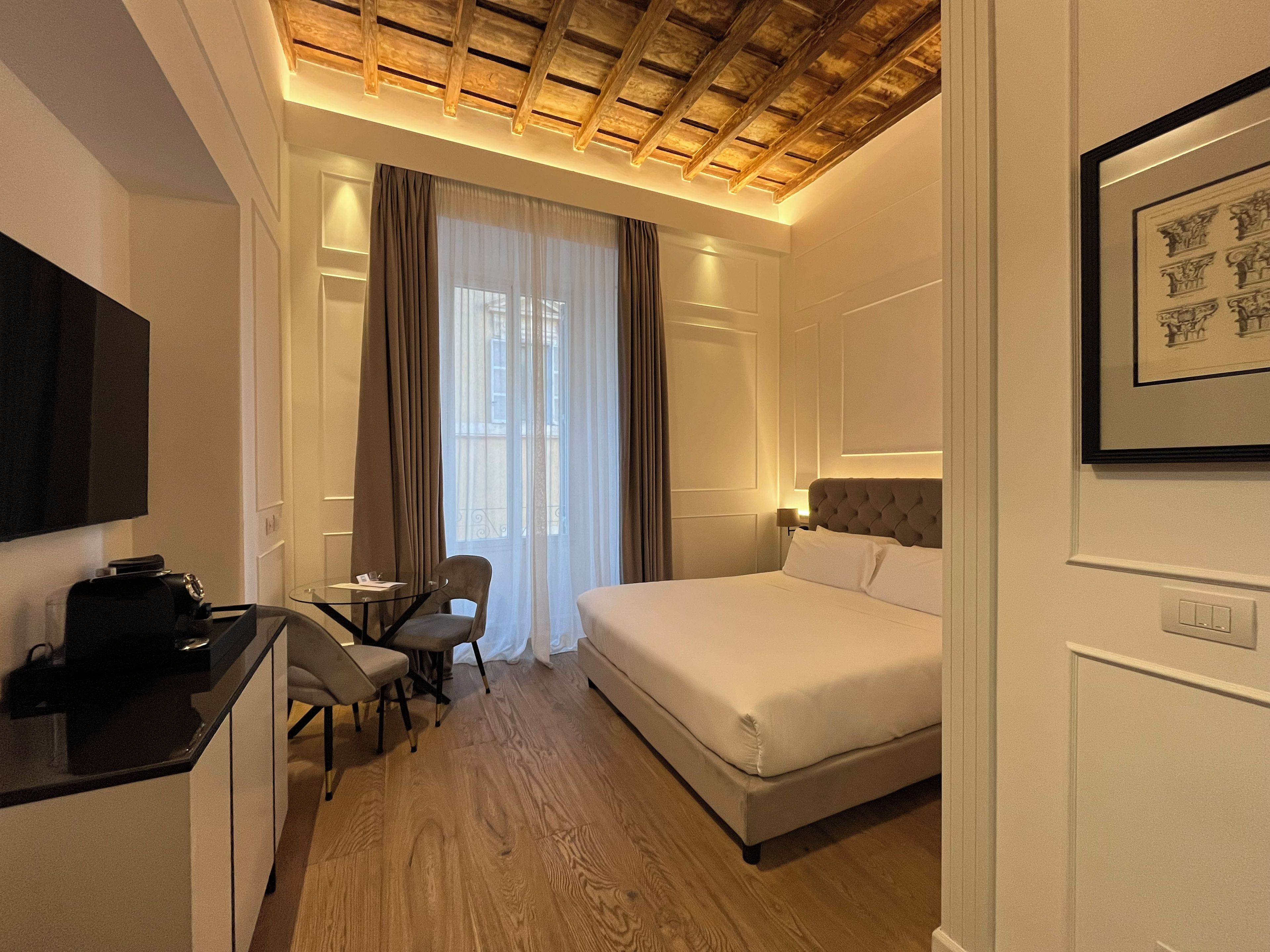 A hotel room with a bed, a desk with a chair, a television, and a framed picture on the wall.