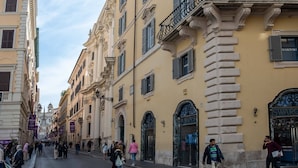 A street lined with historic buildings, including a store with a 'SWAROVSKI' sign. - Palazzo Goldoni Condotti Collection (Rome)