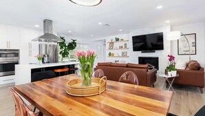 A modern kitchen with white cabinets, a stainless steel range hood, and a dining area with a wooden table and chairs. - Boca Family Fun & Charm - Villa Near Downtown & Beach (Boca Raton)