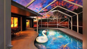 A swimming pool with a swan float, a covered patio, and a sunset view. - Boca Family Fun & Charm - Villa Near Downtown & Beach (Boca Raton)