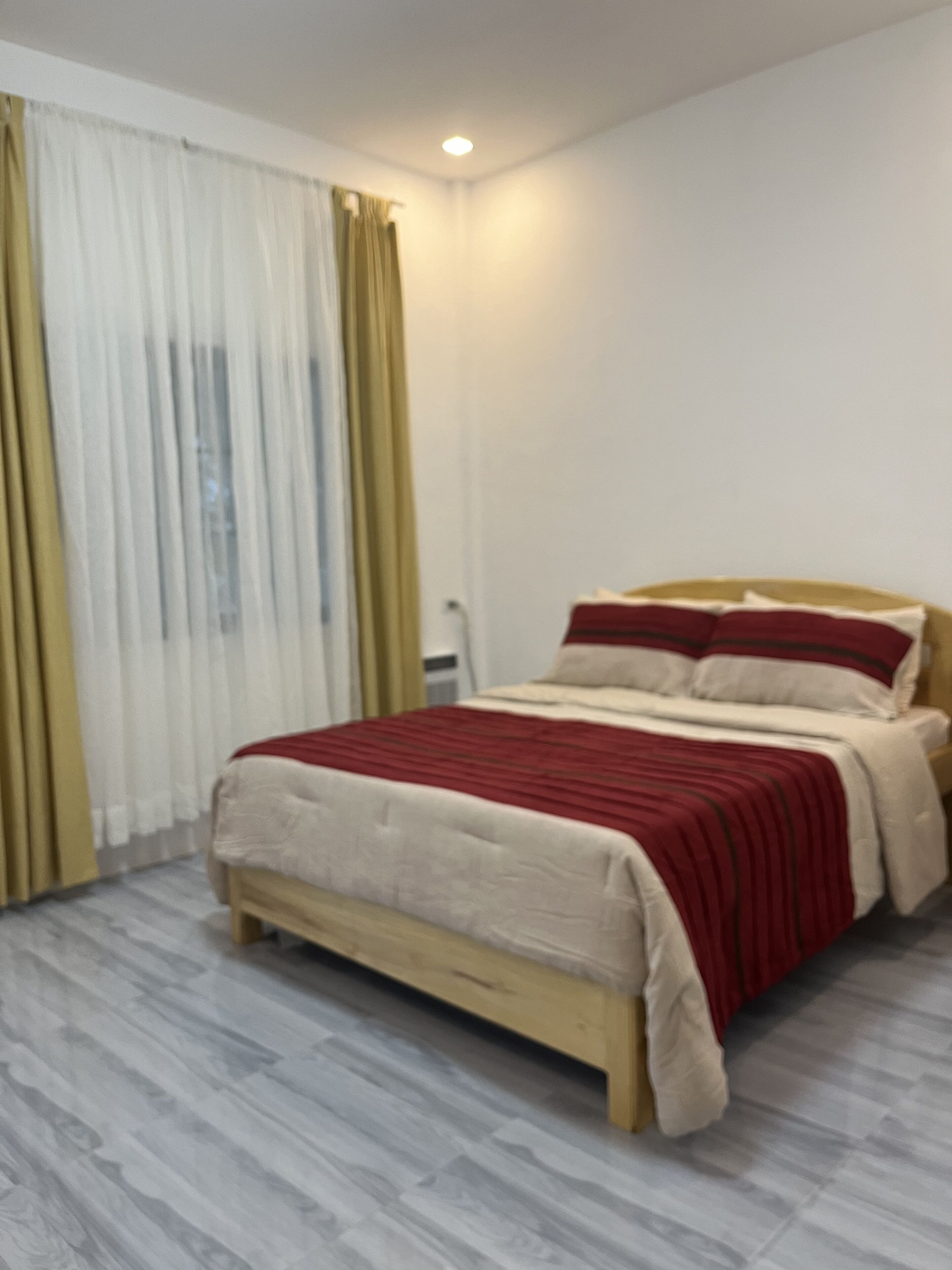 A bedroom with a bed, curtains, and a wooden floor.