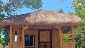 A small wooden structure with a thatched roof, a window, and a door with a decorative emblem. - Maxbelle Mountain Resort (Daanbantayan)