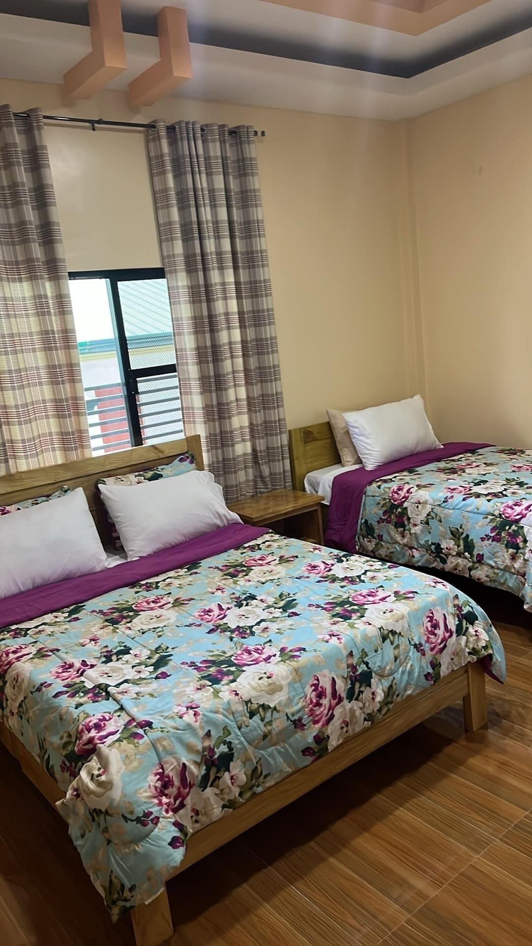A room with two beds, each with floral bedding, wooden headboards, and nightstands.
