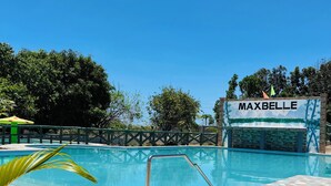 A swimming pool with a tiled deck, surrounded by greenery and a sign reading "MAXBELLE". - Maxbelle Mountain Resort (Daanbantayan)
