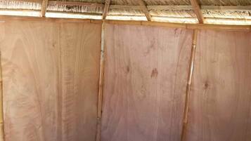 A small, single-room structure with a thatched roof and a ceiling fan.