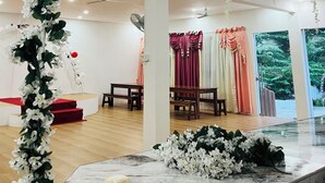 A spacious room with a marble reception desk, a red carpet leading to a seating area, and a view of a forest through a large window.