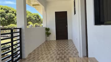 Un couloir couvert avec un sol à carreaux, une plante en pot et une porte au fond.