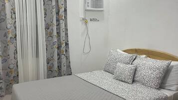A bedroom with a bed, curtains, an air conditioning unit, and a power outlet.