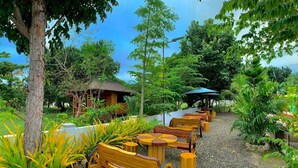 A pathway lined with wooden benches and tables, surrounded by lush greenery and trees.