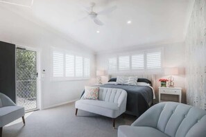 A bedroom with a bed, two chairs, a nightstand, and a ceiling fan.
