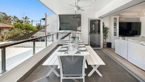 Een modern balkon met een eettafel voor zes personen, een plafondventilator en een aan de muur bevestigde televisie.