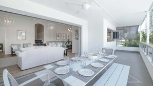 Een moderne eethoek met een lange tafel voor zes personen, een witte bank en een plafondventilator.