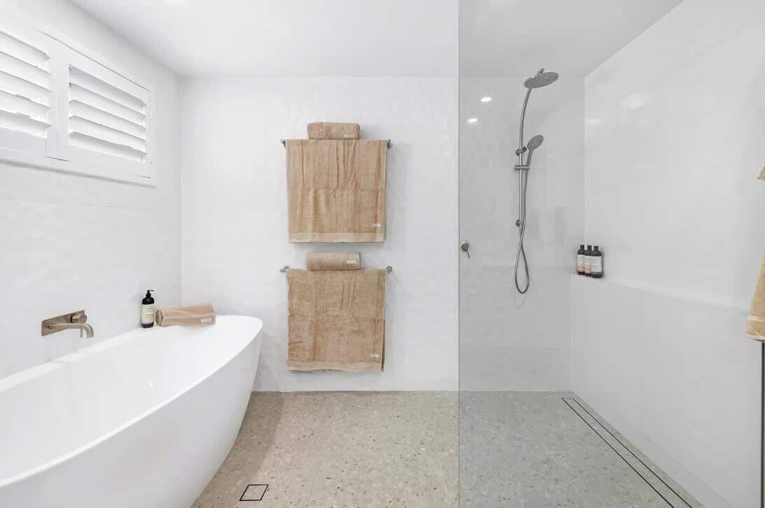 Ein modernes Badezimmer mit einer freistehenden Badewanne, einer begehbaren Dusche mit Glaswand und zwei hölzernen Handtuchhaltern.