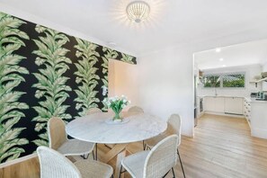 Un coin repas avec une table ronde, des chaises en osier et un mur orné d’un motif de feuilles en noir et blanc.