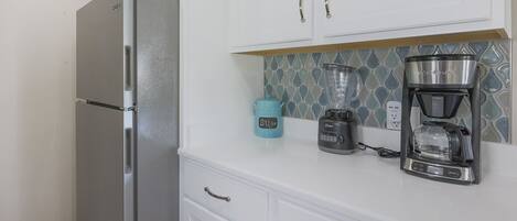 Una cocina con gabinetes blancos, un refrigerador de acero inoxidable, una licuadora y una cafetera.