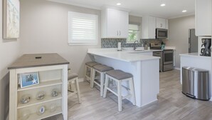 A modern kitchen with white cabinetry, a central island with stools, a built-in oven, and a stainless steel refrigerator.