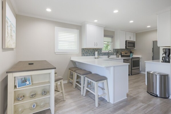 A modern kitchen with white cabinetry, a central island with stools, a built-in oven, and a stainless steel refrigerator.