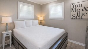 A bedroom with a large bed, two bedside tables with lamps, a dresser, and a wall with a motivational quote.