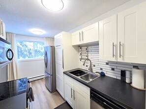 Una cocina moderna con armarios blancos, encimera negra, pileta de acero inoxidable y ventana con cortinas.