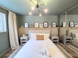 Habitación de hotel ordenada con una cama grande, mesitas de noche, un espejo y cuadros en la pared.