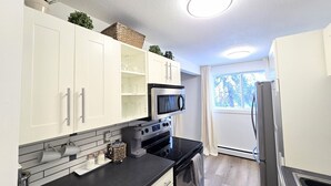 Eine moderne Küche mit weißen Schränken, einer schwarzen Arbeitsplatte, Edelstahlgeräten und einem Fenster, das für natürliches Licht sorgt.