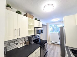 A modern kitchen with white cabinets, a black countertop, stainless steel appliances, and a window providing natural light. - 2 Bedroom Suite Downtown w/ Parking (Edmonton)
