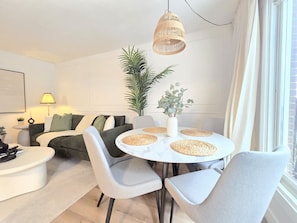 Una sala de estar moderna con una mesa de comedor redonda, sofás grises y un ventanal con cortinas.