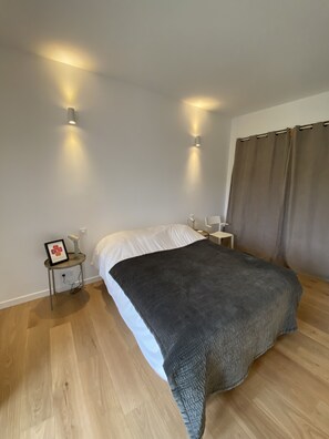 A bedroom with a bed, bedside tables, a nightstand, a framed picture, and a window with curtains. - Ancien Moulin en Pierre (Saint-Pierre-de-Vassols)