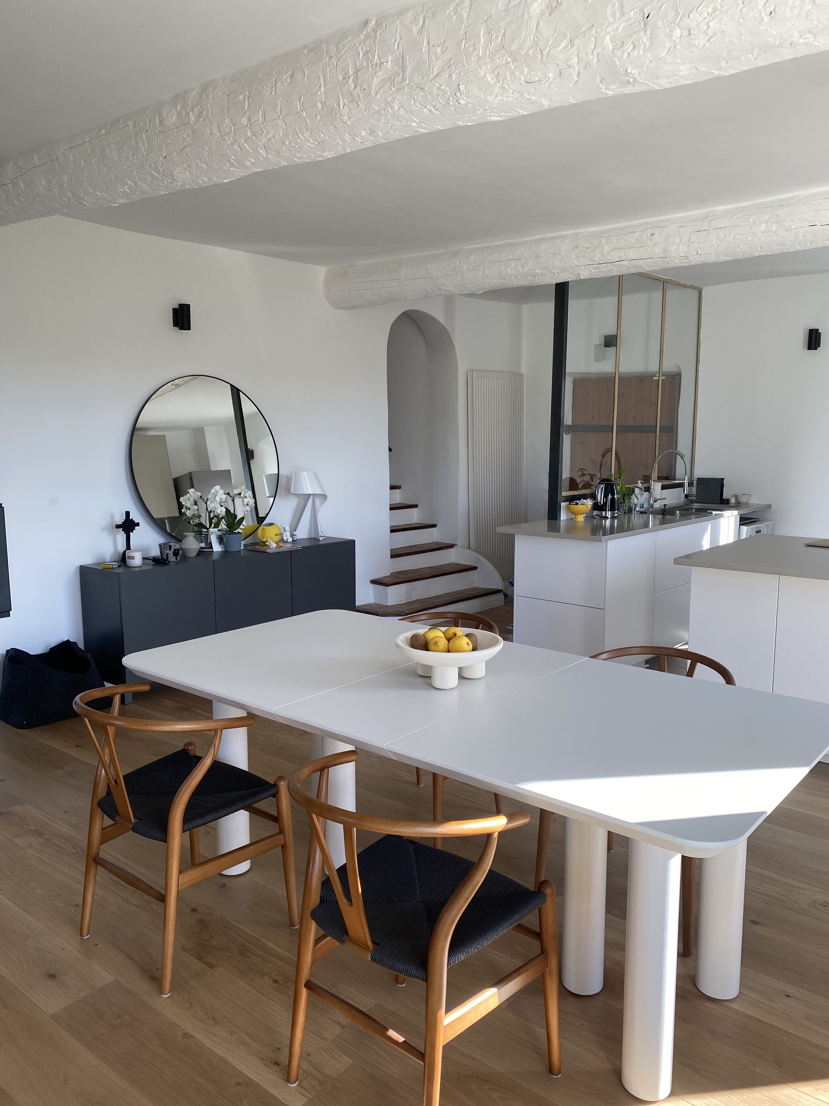 Une cuisine moderne avec des meubles blancs, un îlot central et un coin repas comprenant une table blanche et des chaises en bois.