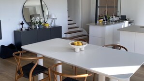 Une cuisine moderne avec des meubles blancs, un îlot central et un coin repas comprenant une table blanche et des chaises en bois.