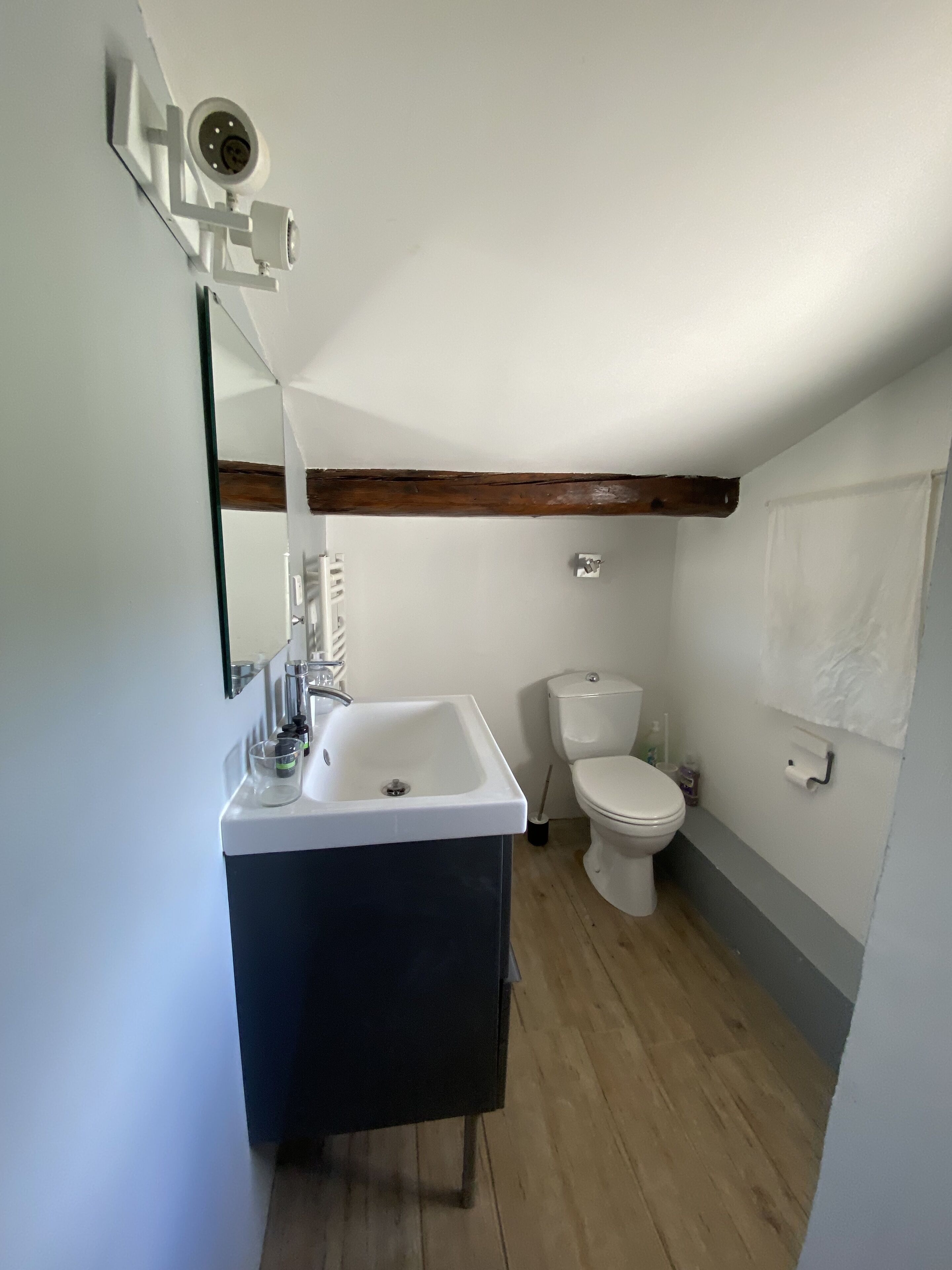 Une petite salle de bain avec un lavabo blanc, des toilettes et une caméra de surveillance fixée au mur.