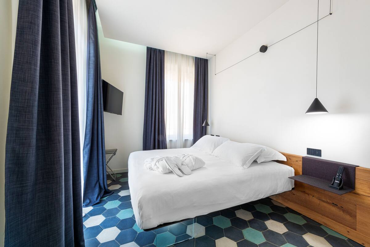 Quarto de hotel moderno com uma cama grande, televisão montada e um padrão de piso hexagonal único.