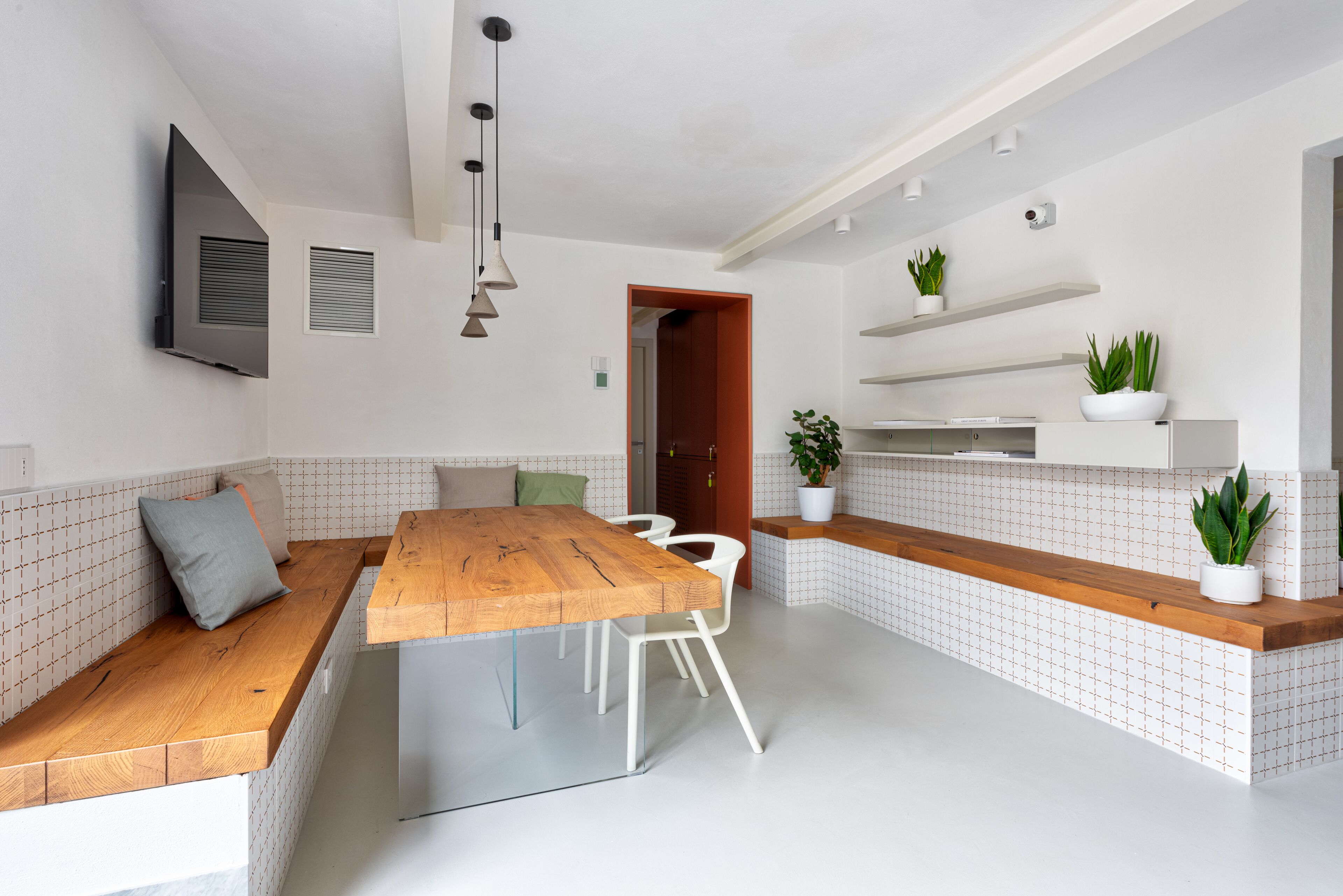 Una cocina moderna con una mesa de comedor de madera, sillas blancas, un banco empotrado y plantas en macetas.