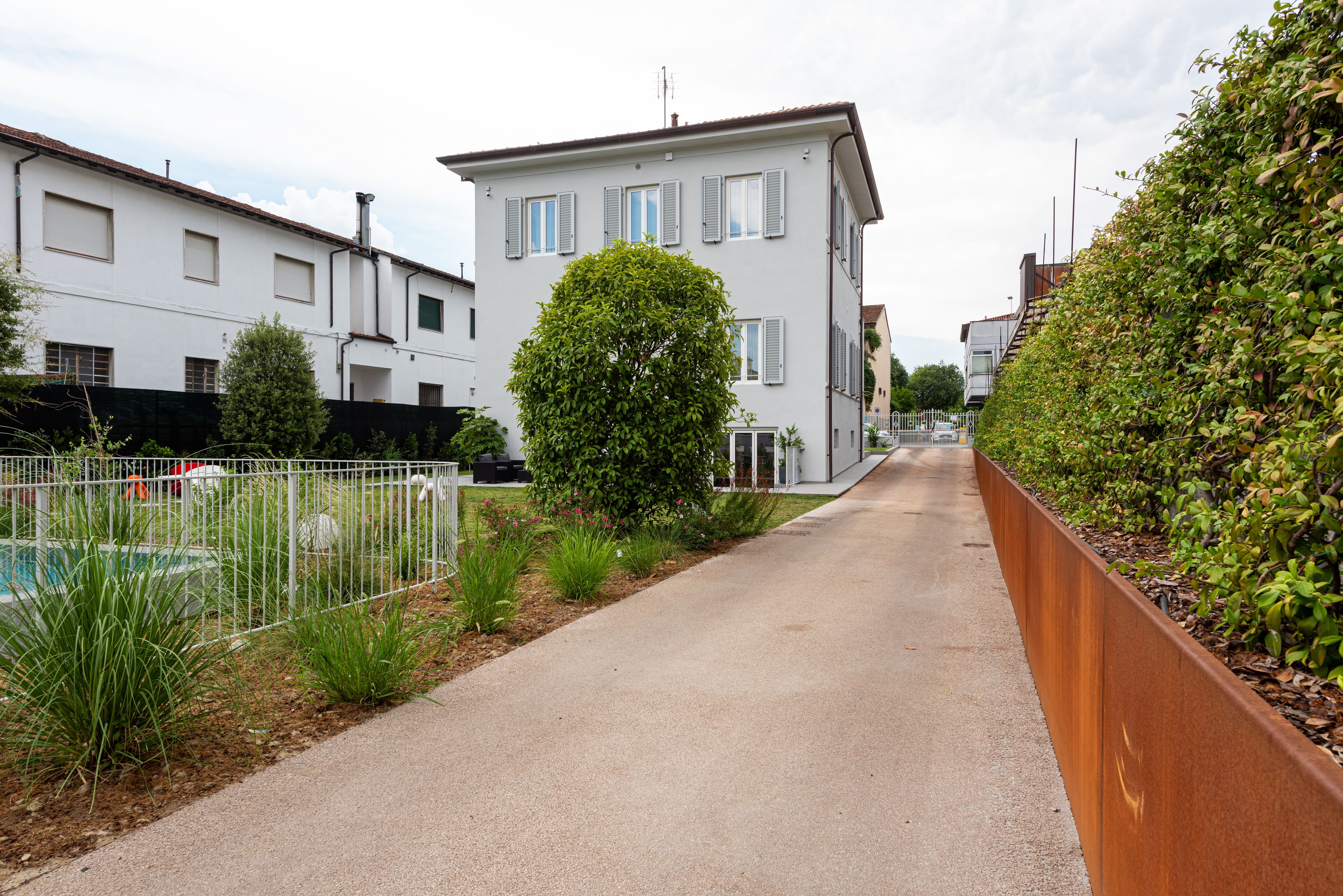 A residential street with houses, a sidewalk, and a metal fence.