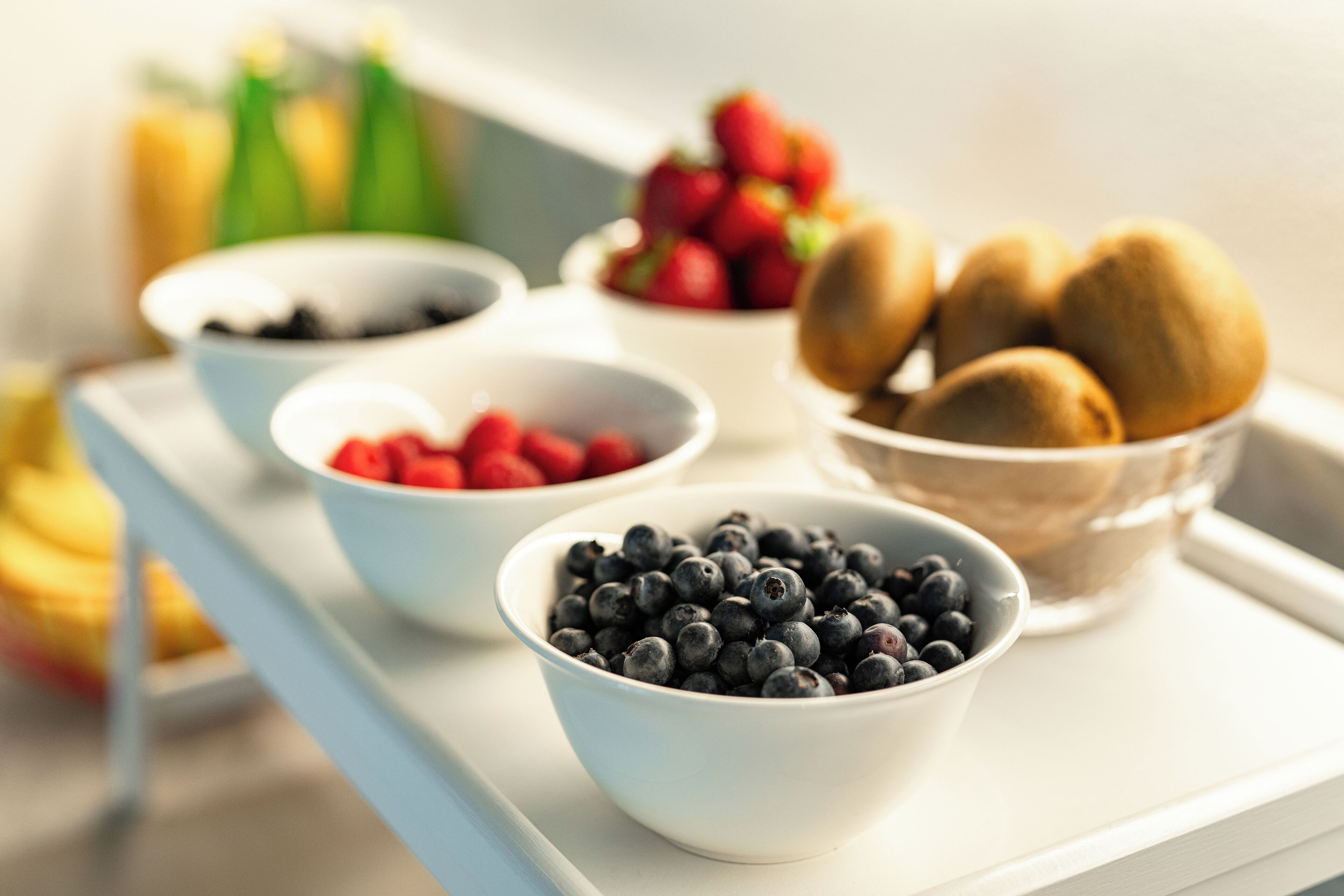A tray with bowls containing blueberries, raspberries, and kiwis.