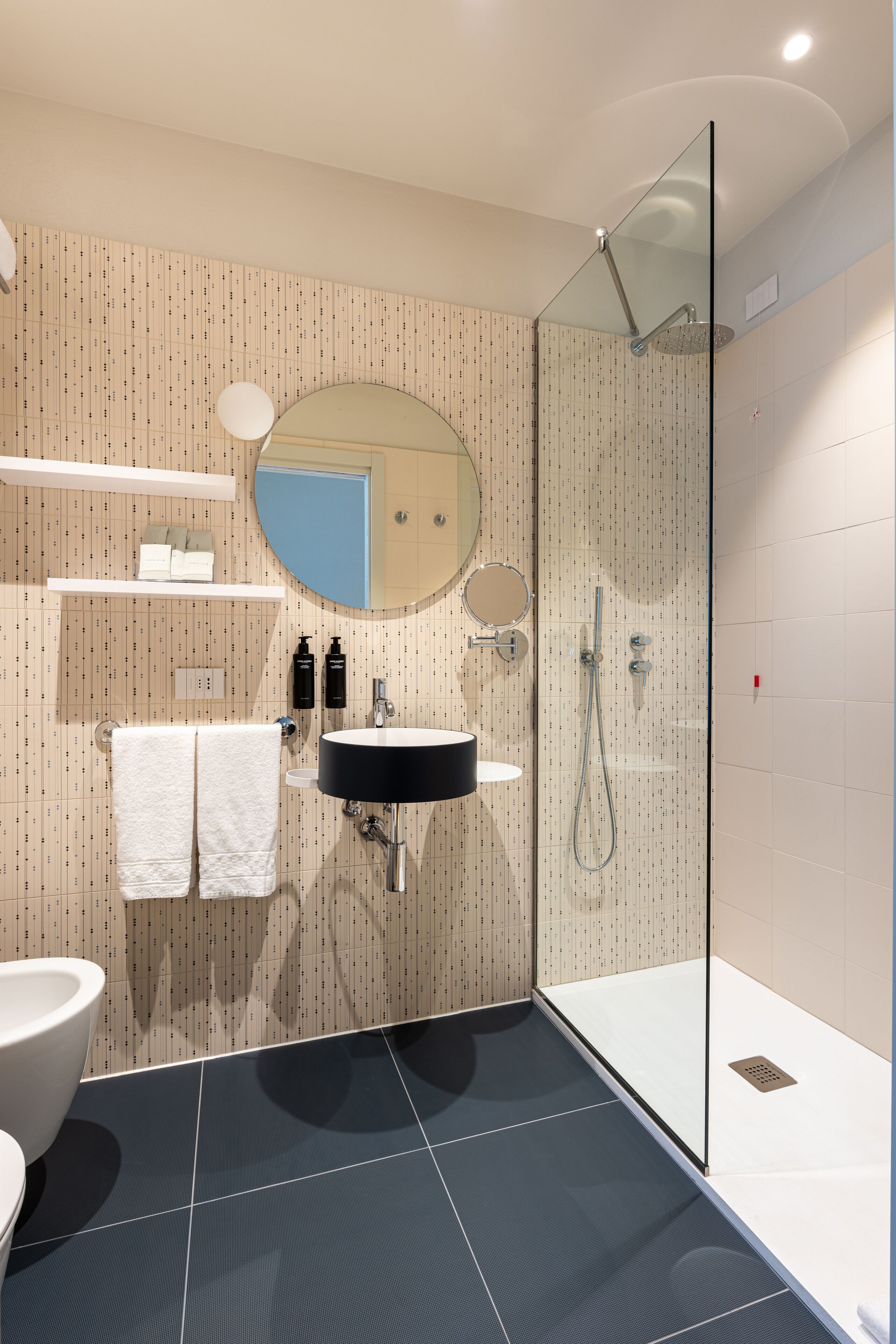 A modern bathroom with a glass-enclosed shower, a sink with a black basin, and a mirror above it.