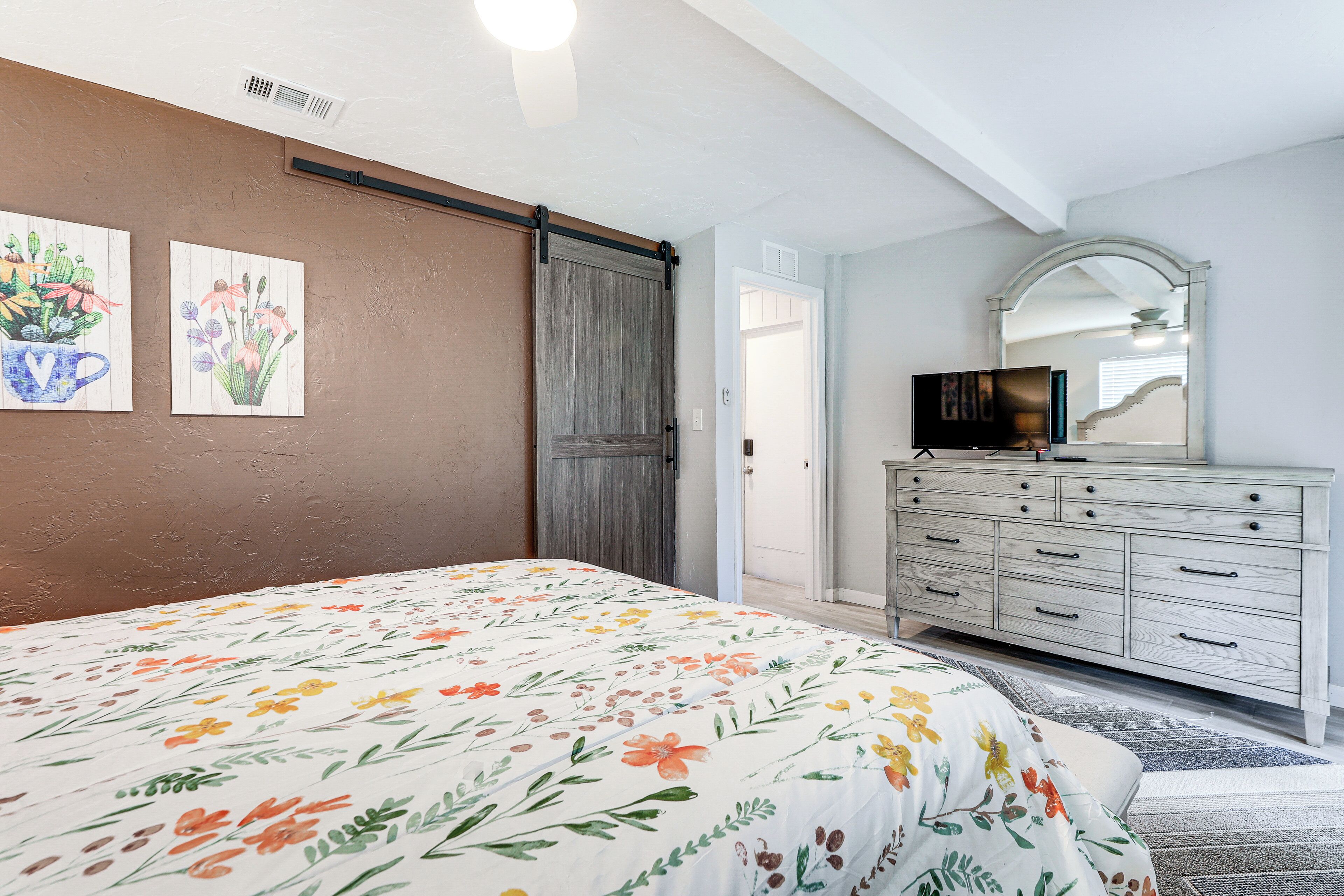 Un dormitorio con colcha estampada, un aparador, un televisor y un espejo.