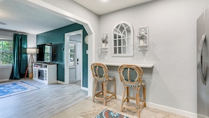 A spacious living area with a teal accent wall, a white fireplace, two wicker chairs, and a blue rug. - Idyllic Sarasota Home w/ Yard: 2 Mi to Beach! (Sarasota)