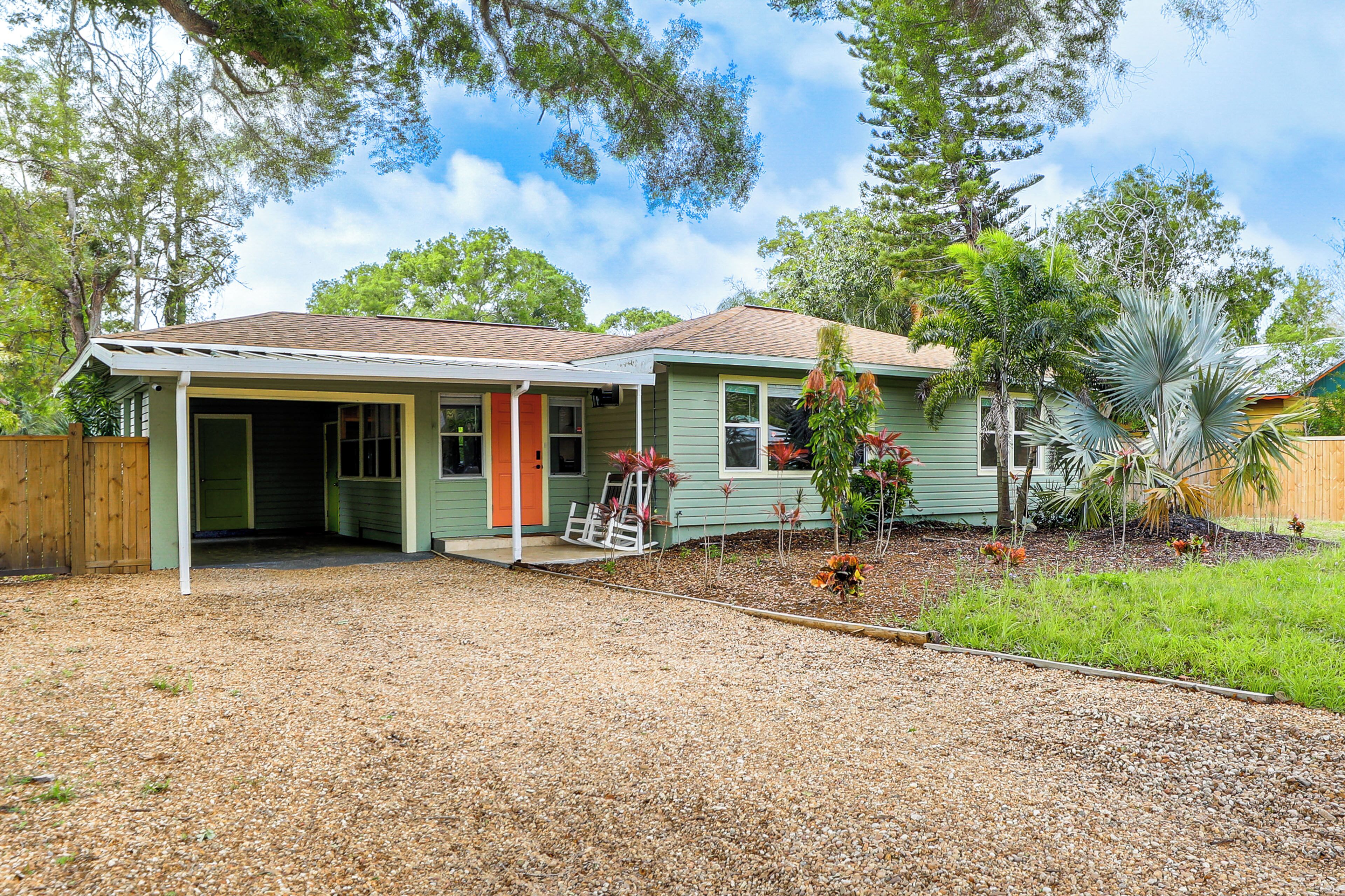 A single-story house with a covered porch, a fenced yard, and a gravel driveway.