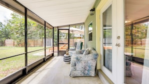 A covered porch with a sofa and ottoman, large windows, and a view of a backyard. - Idyllic Sarasota Home w/ Yard: 2 Mi to Beach! (Sarasota)