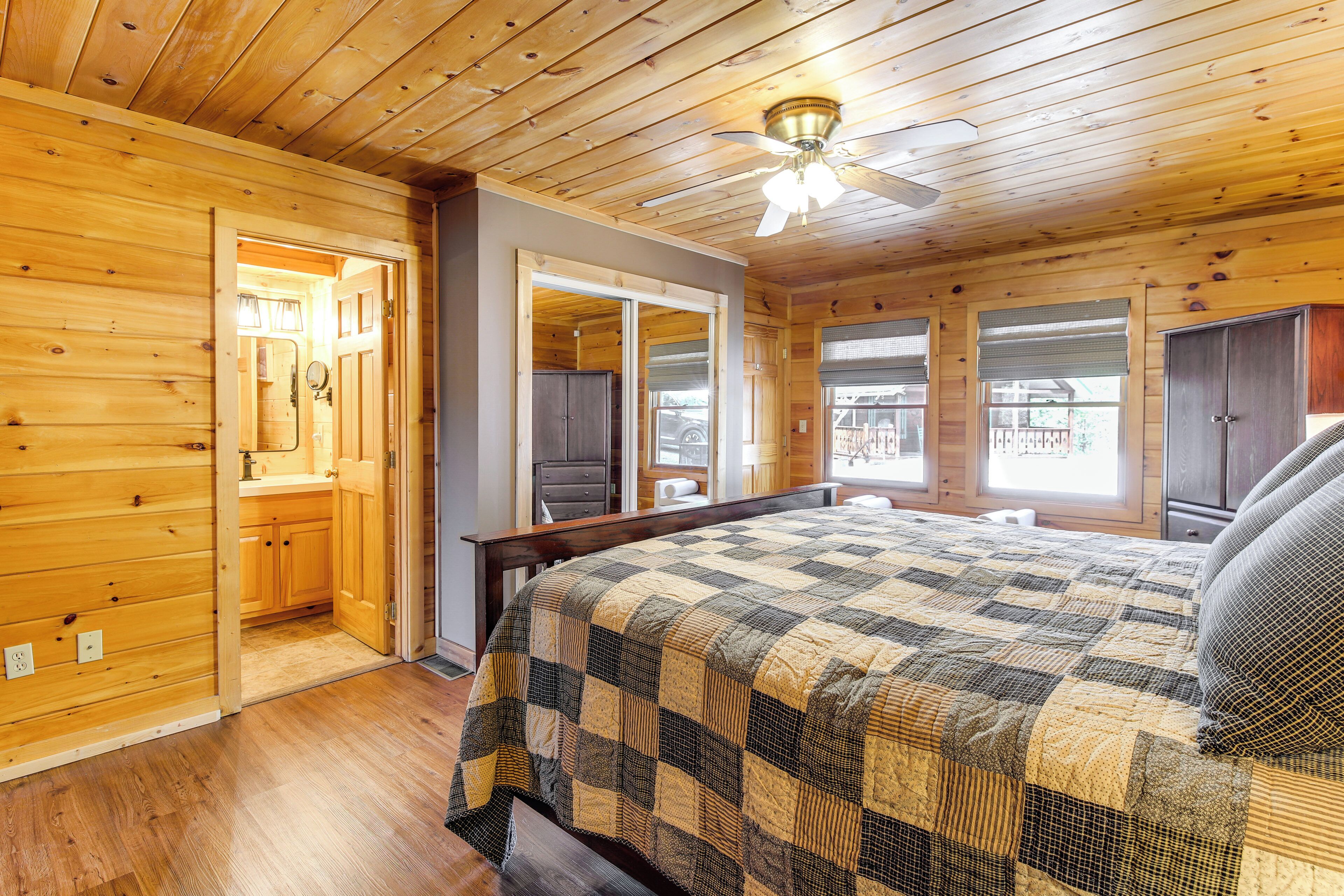 A wooden cabin bedroom with a bed, a ceiling fan, and a large window.