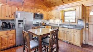 A wooden cabin-style kitchen with a central island, stainless steel appliances, and a stone backsplash. - Cozy Sevierville Cabin w/ Hot Tub, Mountain Views! (Sevierville)