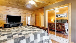A wooden cabin bedroom with a bed, a television, and a sliding door leading to a balcony. - Cozy Sevierville Cabin w/ Hot Tub, Mountain Views! (Sevierville)