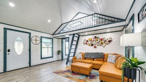 A spacious living room with a large sectional sofa, a wooden floor, a staircase, and a decorative wall piece.