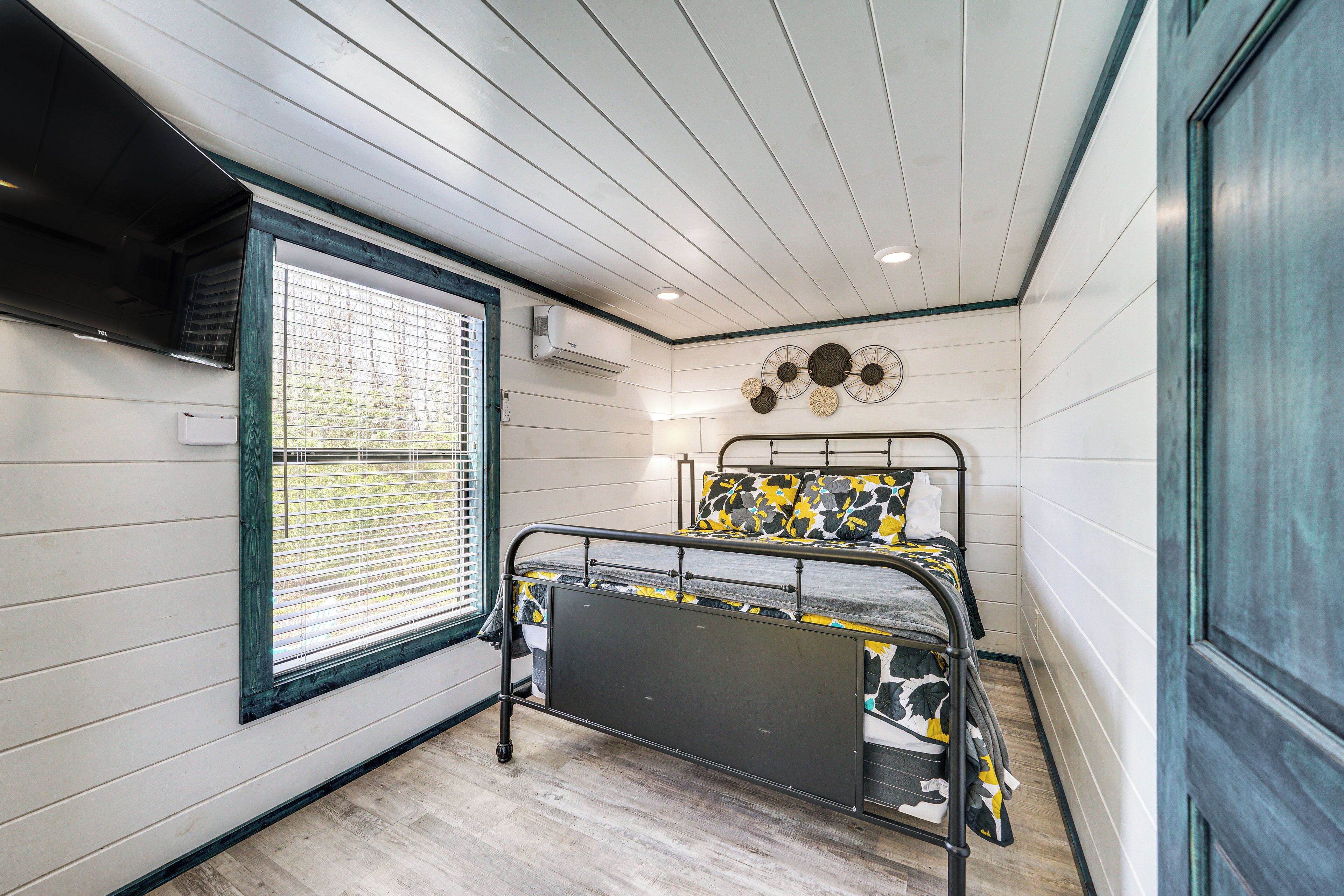 Une chambre à coucher de taille réduite, équipée d’un lit superposé, d’une fenêtre avec stores, d’un ventilateur de plafond et d’un climatiseur fixé au mur.